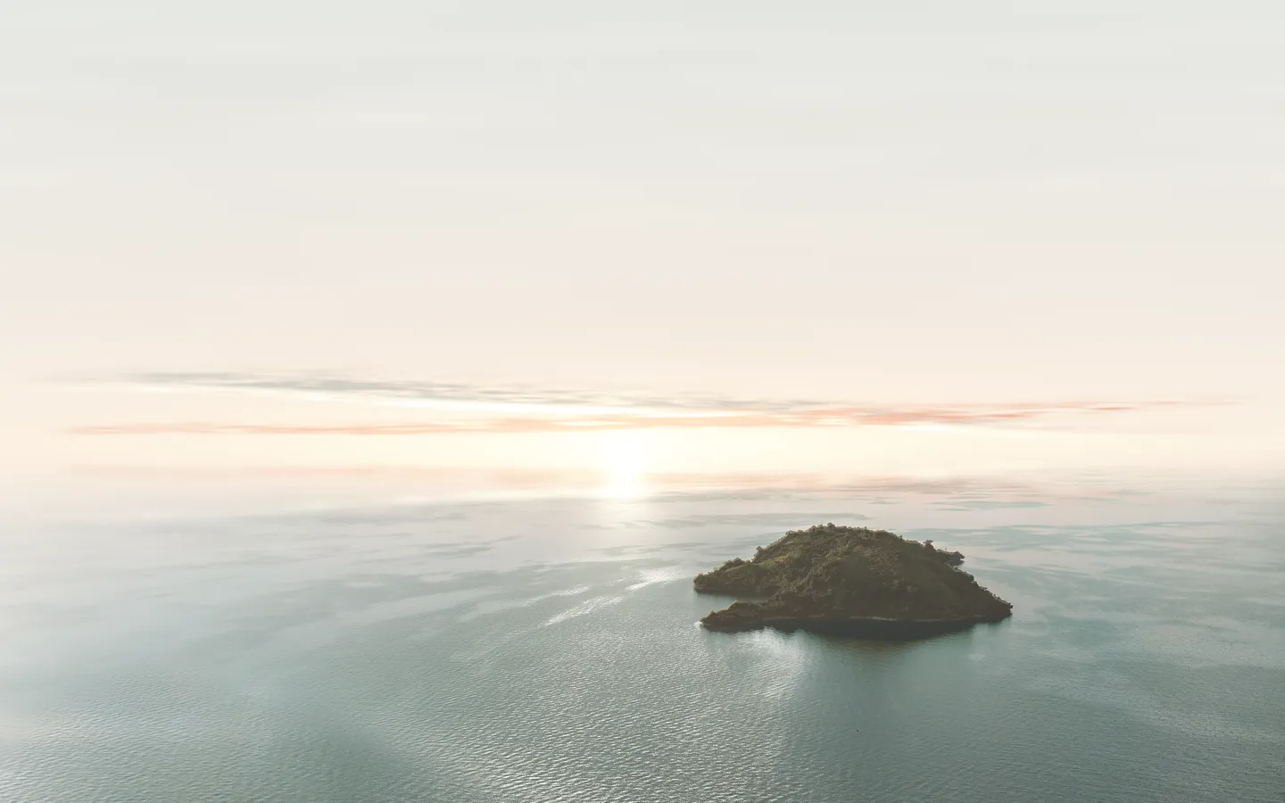 Lake Kivu at first light: a forested island in the lake, a low sun in the haze on the horizon, and its light on the water